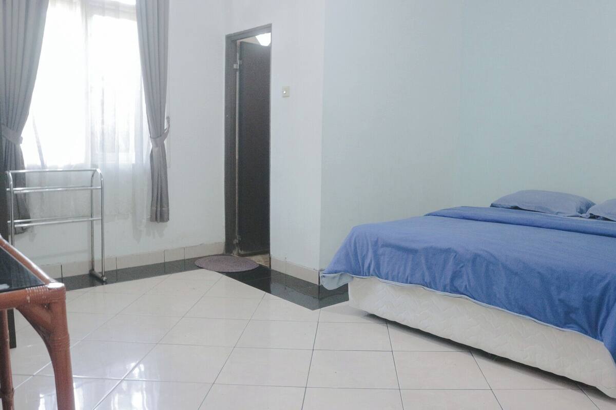 A bedroom with a bed, a chair, a door, and a tiled floor.