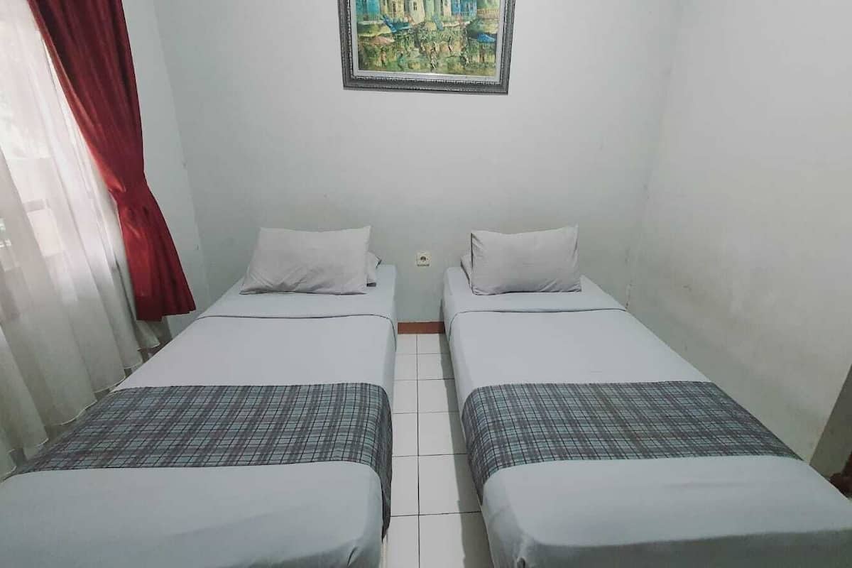 A small, clean room with two single beds, a window with red curtains, and a painting on the wall.