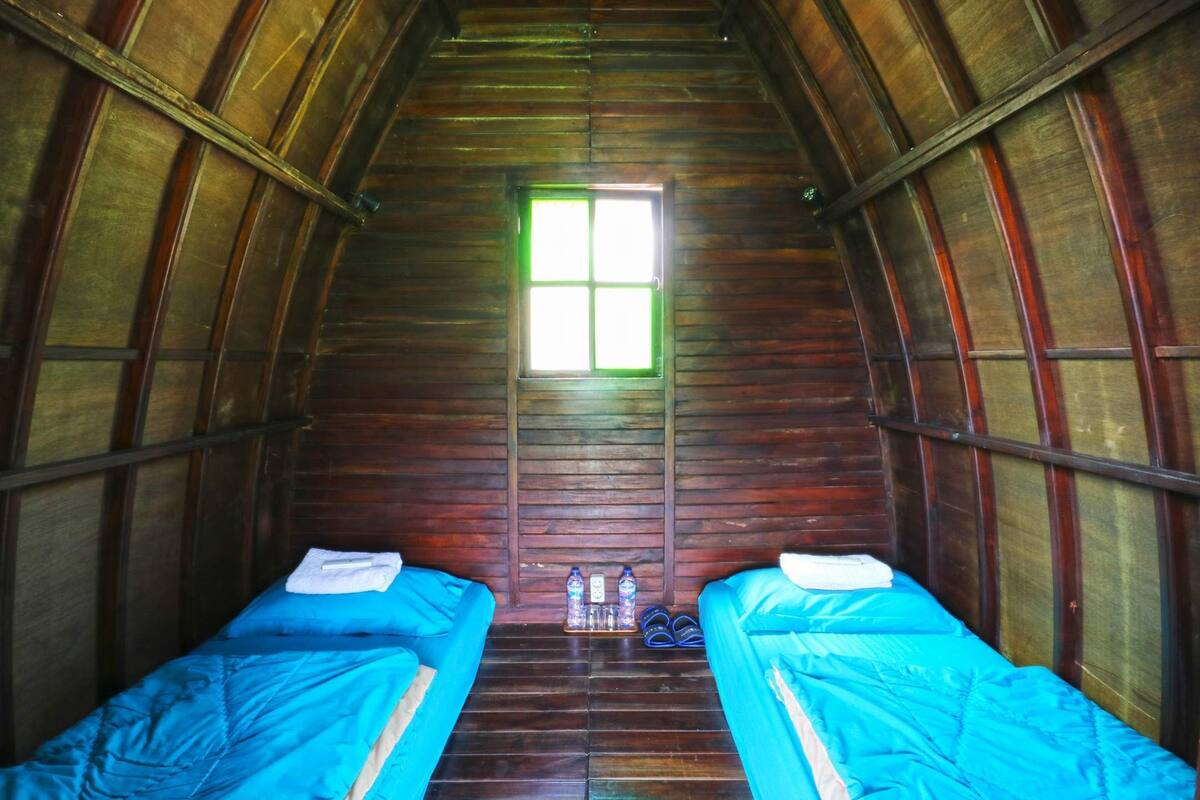 A wooden cabin with two beds, a window, and a pair of shoes on the floor.