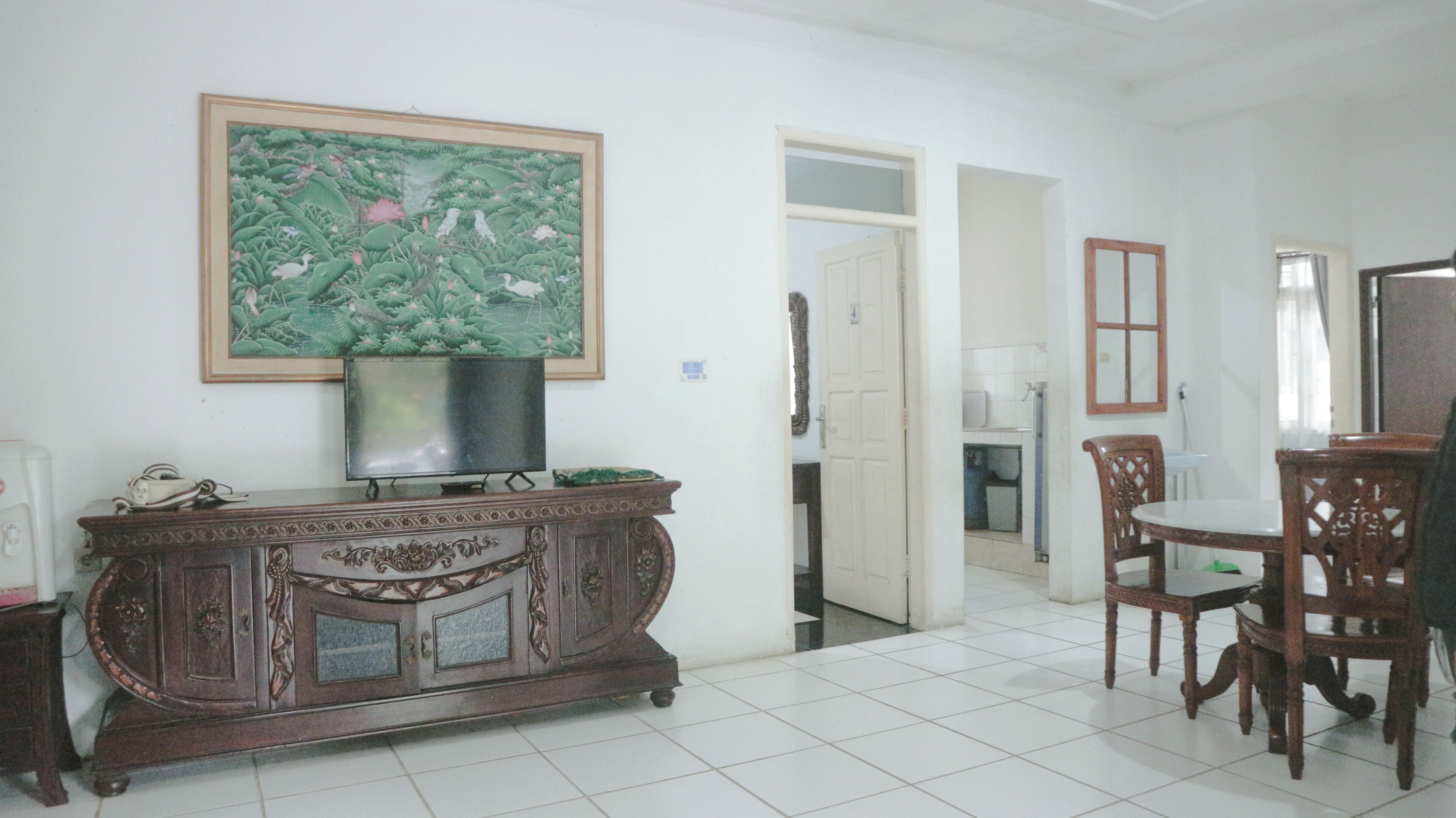 A dining area with a wooden cabinet, a television, and a framed painting on the wall.