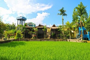A traditional house with a water tower, surrounded by lush greenery and a rice field. - Aries Biru Hotel & Villa (Cisarua)