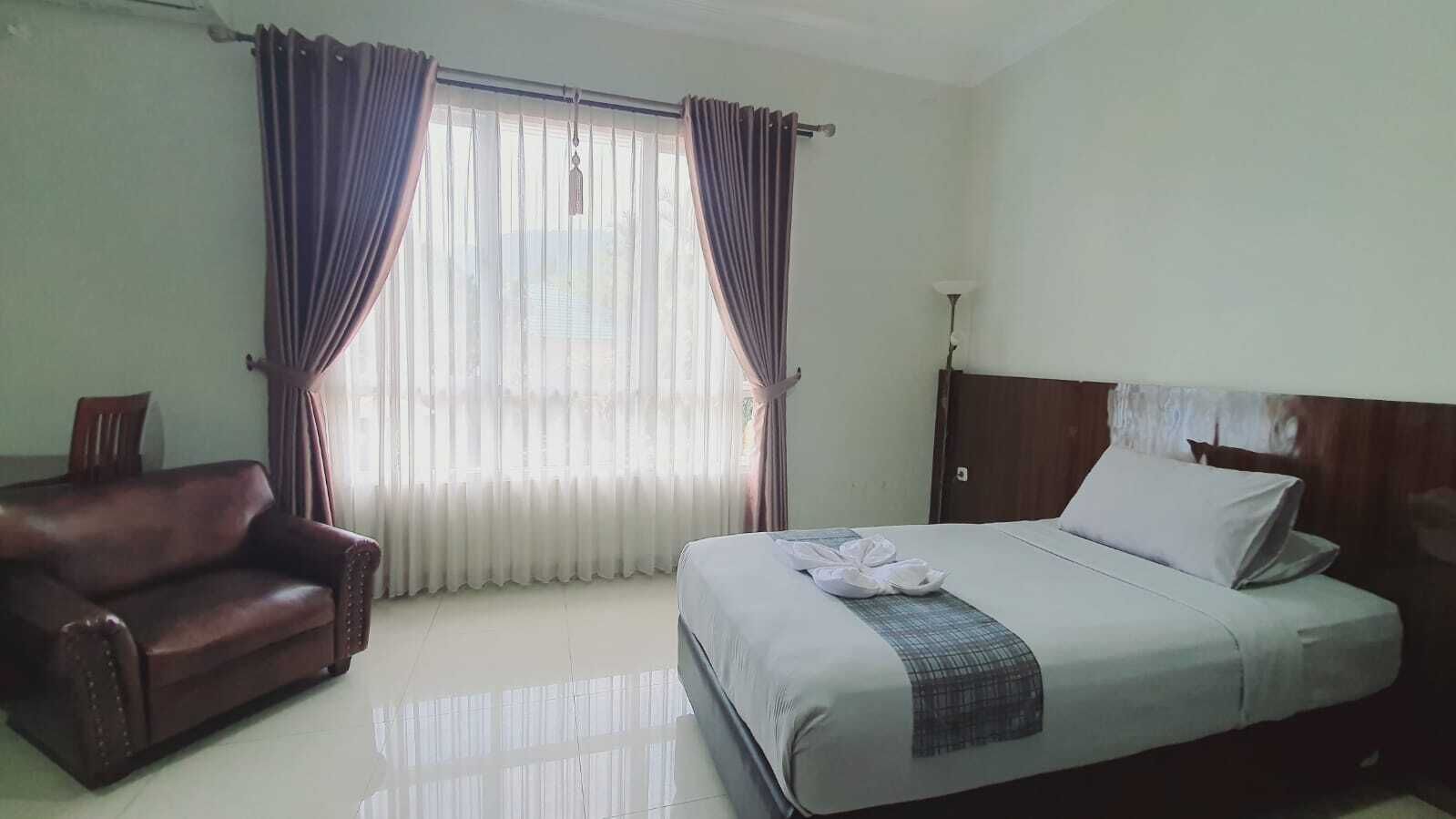 A hotel room with a bed, a chair, and a window with curtains.