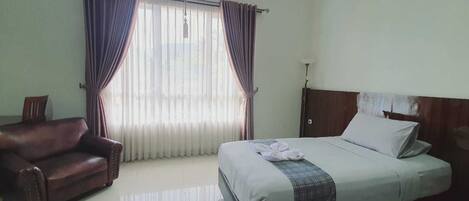 A hotel room with a bed, a chair, and a window with curtains.