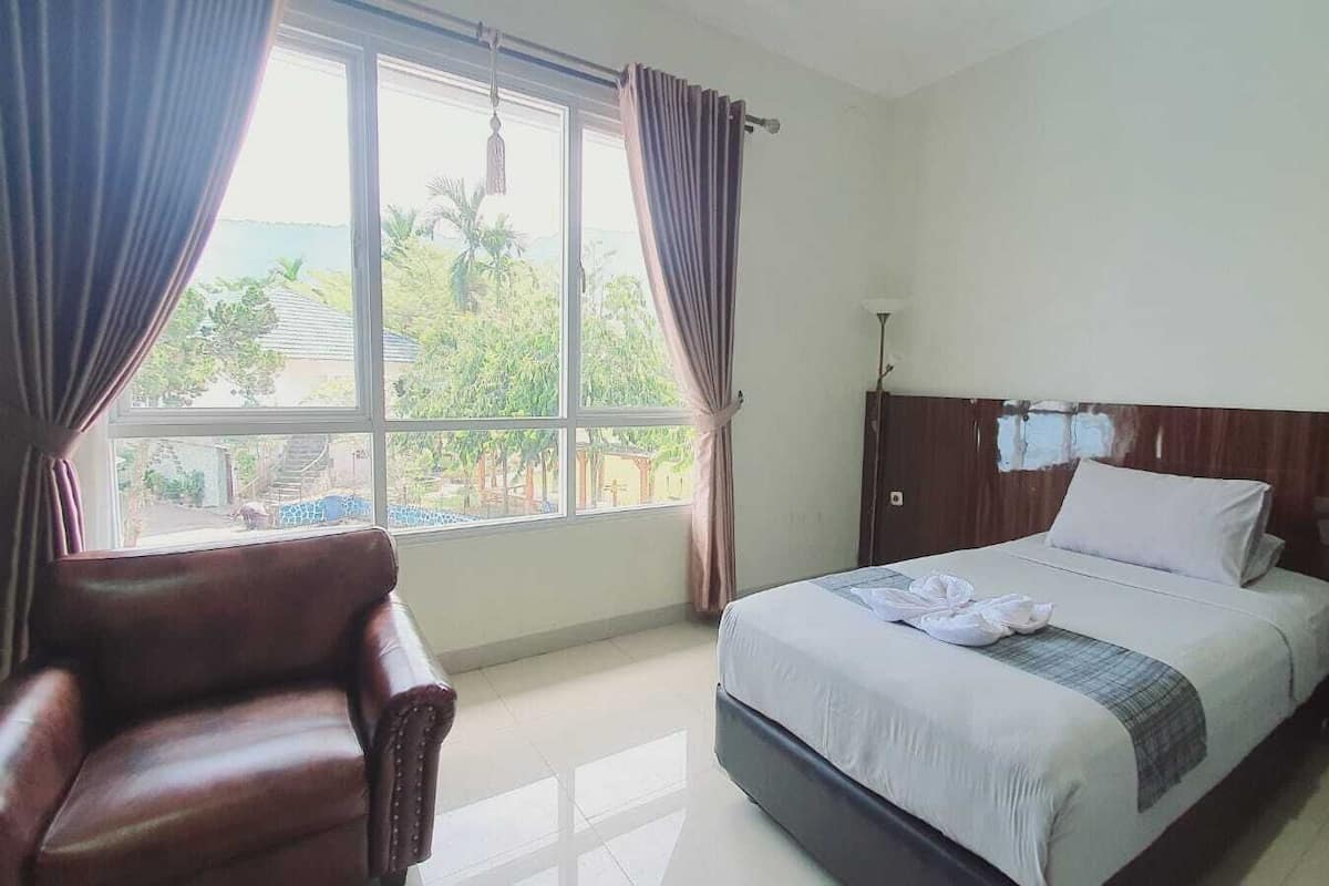 A hotel room with a bed, a chair, and a large window with curtains.