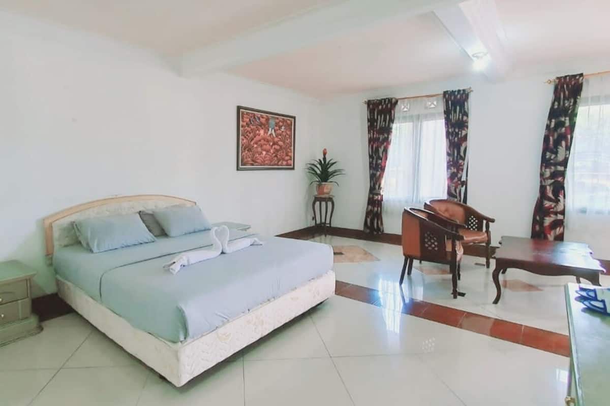 A bedroom with a bed, bedside table, chair, desk, and curtains.