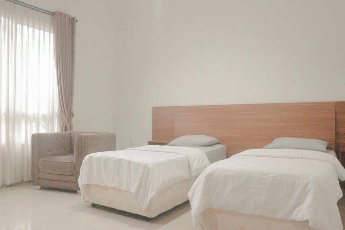 A hotel room with two beds, a chair, and a large window with curtains.