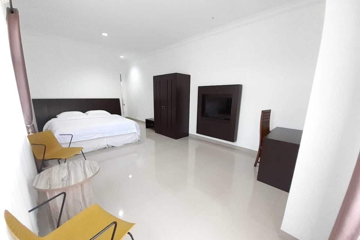 A modern hotel room with a large bed, a TV, a wardrobe, and a small table with chairs.