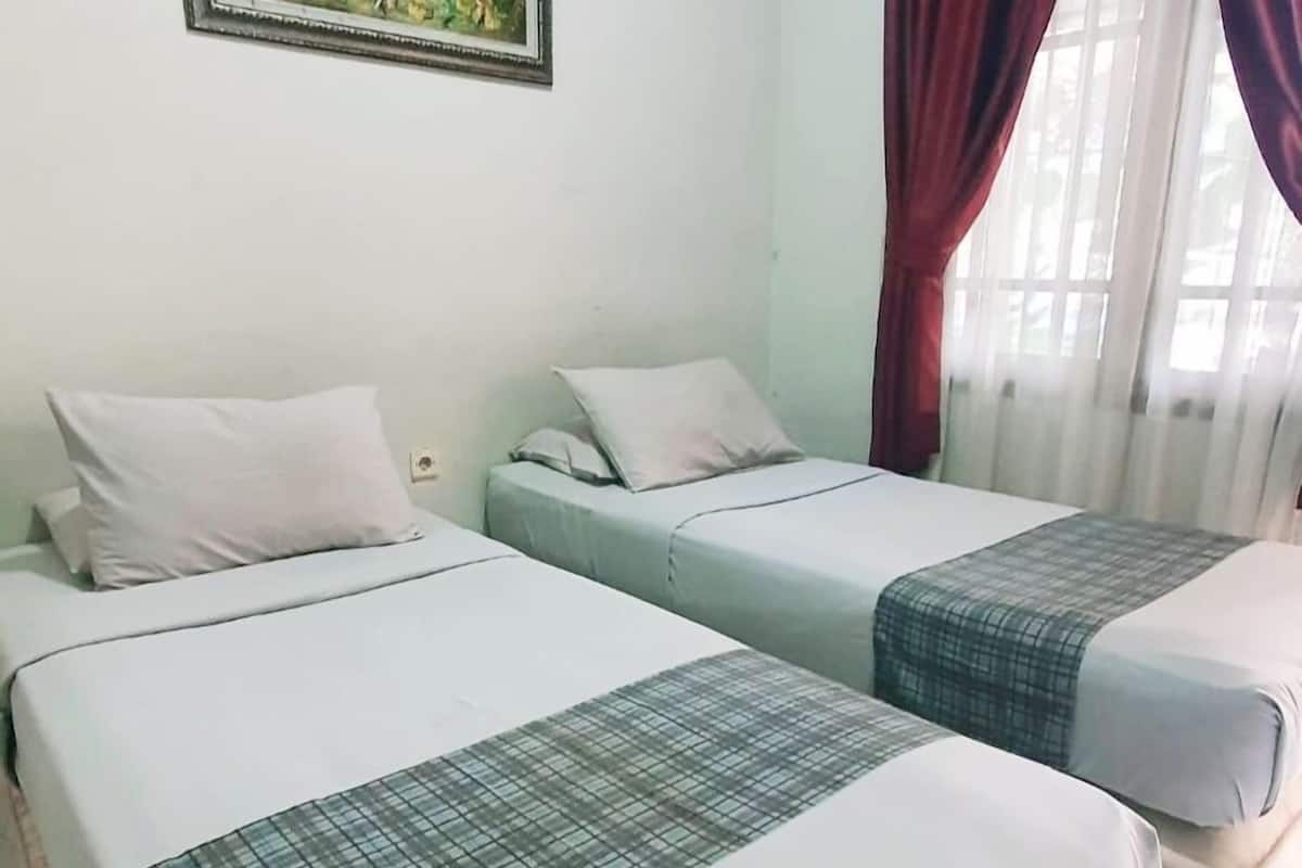 Two single beds with white and grey bedding, a small painting on the wall, and a window with red curtains.