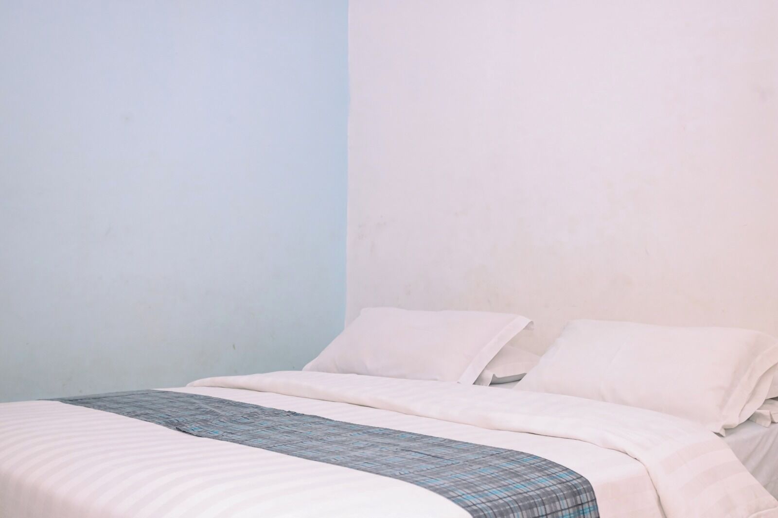 A simple, unadorned room with a bed, plain walls, and a single blanket.