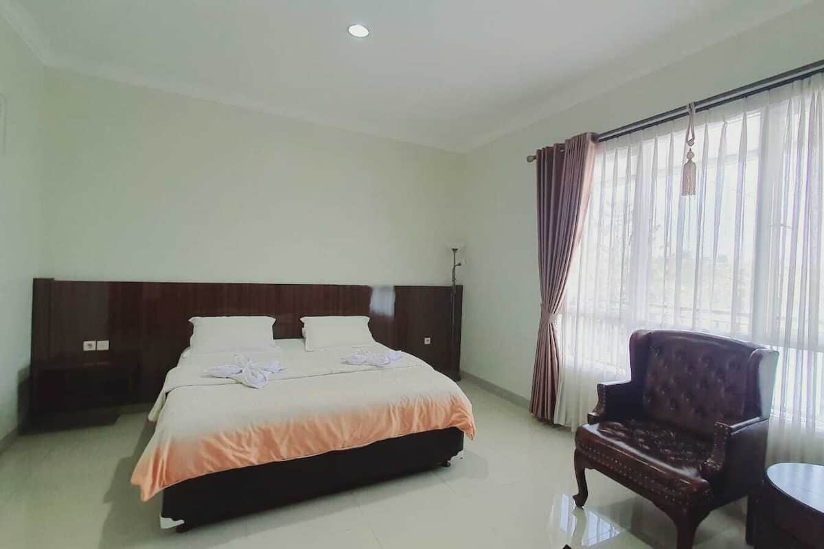 A hotel room with a large bed, a wooden headboard, a chair, and a small table.