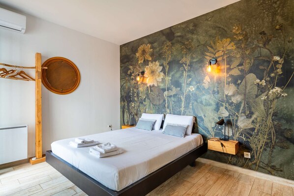 A modern bedroom with a large bed, a wooden wardrobe, a round mirror, and a floral wallpaper.