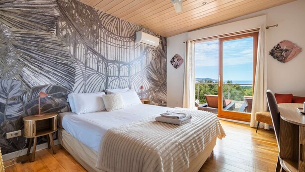 A bedroom with a large bed, a ceiling fan, a view of the outdoors, and a balcony with seating. - Villa Castille – Pool and Sea View in Lumio, Balagne (LUMIO)
