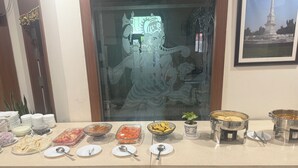 A buffet table with various food items and utensils, a decorative glass door with a figure, and a framed picture of a monument. - Icon Residency Inn (Prayagraj)