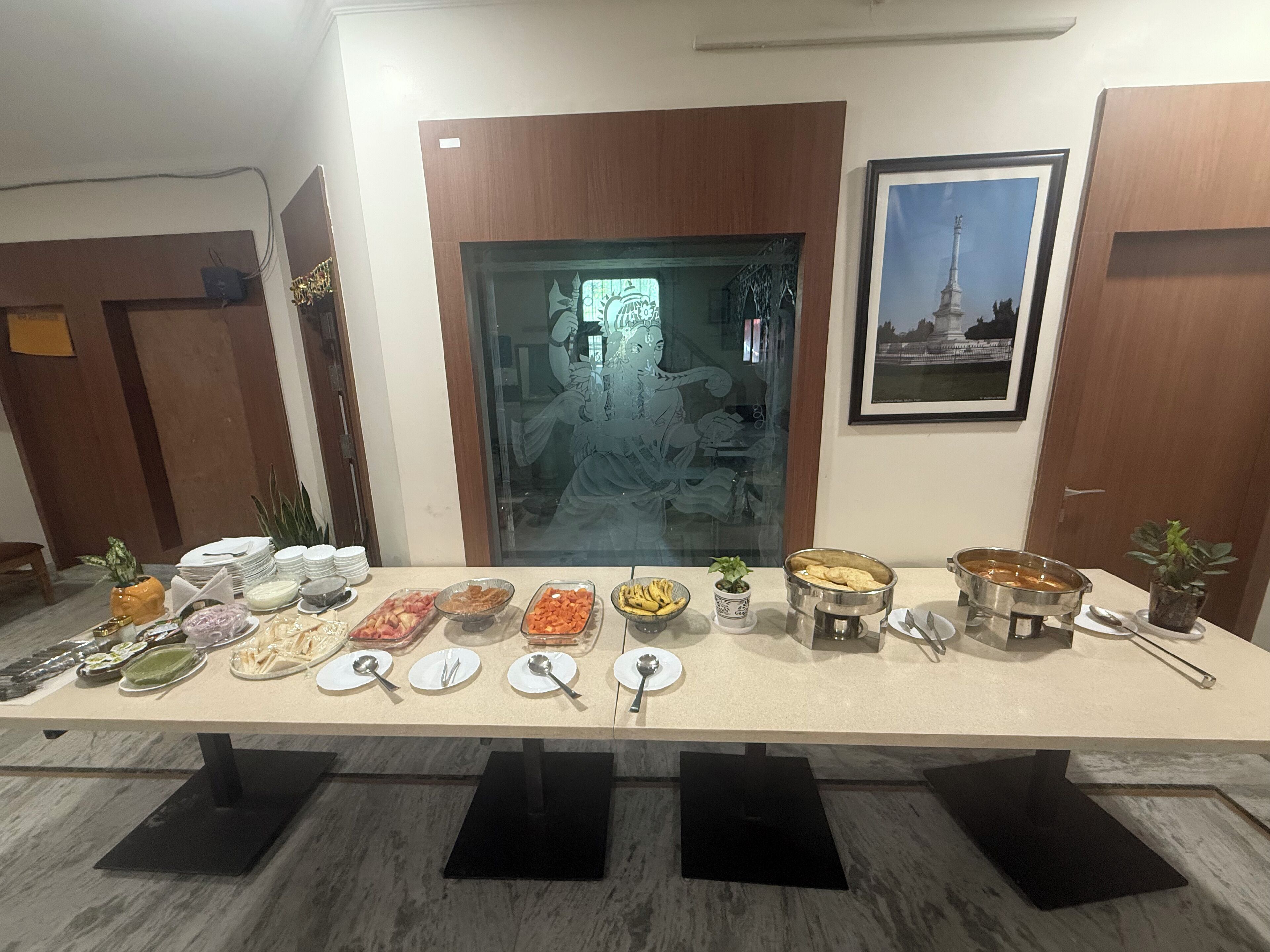 Ein Buffet mit verschiedenen Speisen und Besteck, vor dem Hintergrund eines Raumes mit Holztüren und einem gerahmten Bild an der Wand.