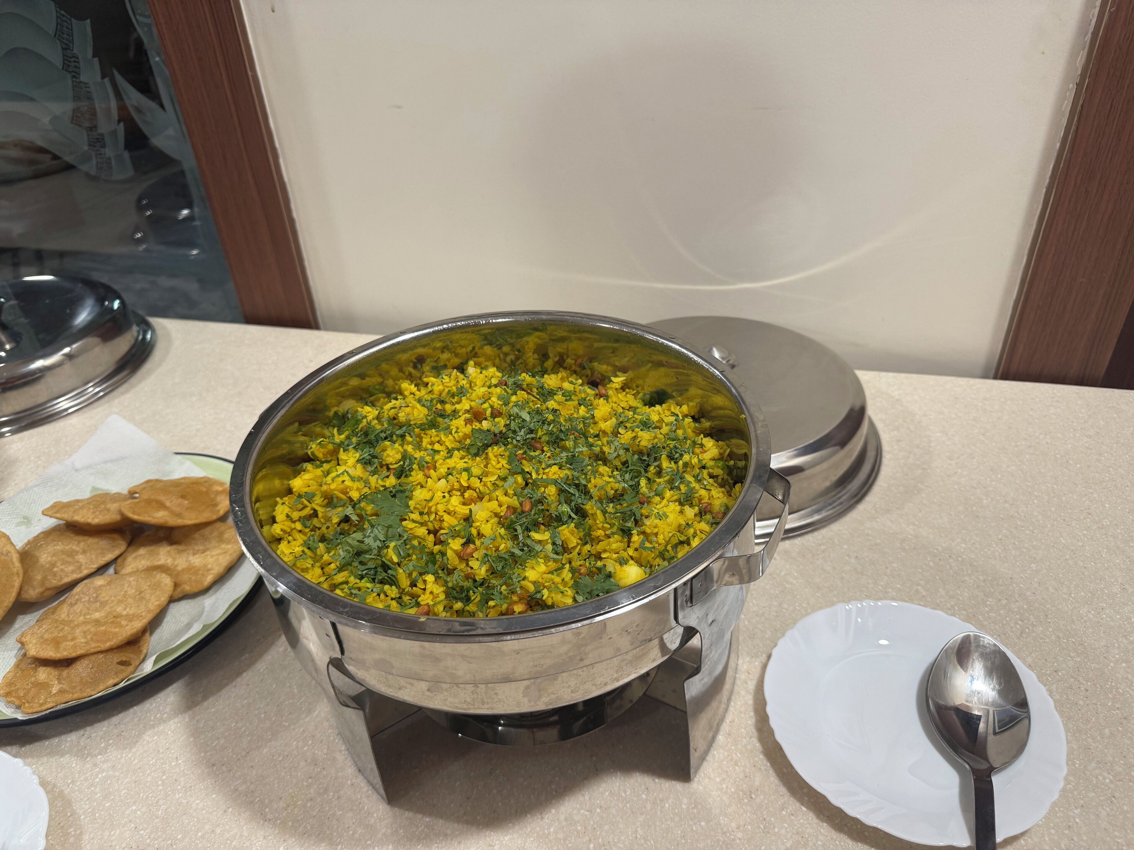 A buffet table with a large pot of yellow rice garnished with herbs, a plate of crackers, and a spoon.