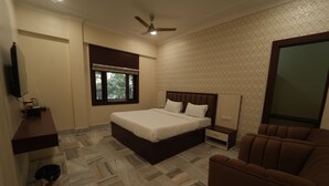 A bedroom with a bed, a ceiling fan, a window, a TV, a bedside table, and a chair. - Icon Residency Inn (Prayagraj)