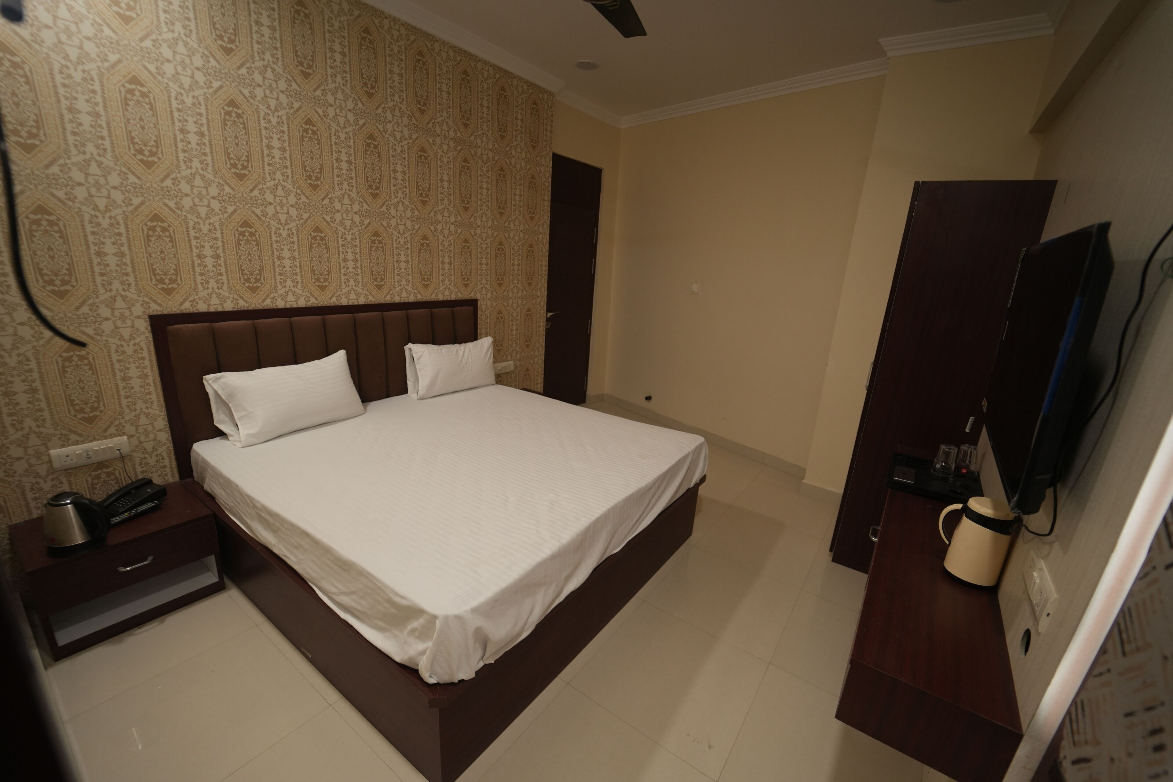 A hotel room with a large bed, a bedside table with a phone and a coffee maker, and a TV on a stand.
