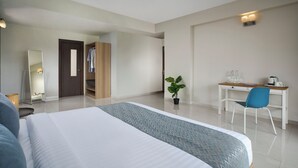 A hotel room with a large bed, a desk with a chair, a mirror, a wardrobe, and a potted plant. - Paprika Stays (Panaji)