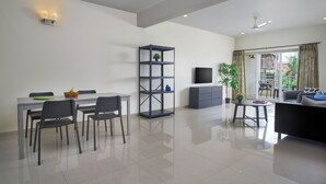 A modern living space with a dining area, a sofa, a TV, and a balcony with a view. - Paprika Stays (Panaji)