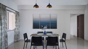 A dining area with a table set for four, two pendant lights, and a large abstract painting on the wall. - Paprika Stays (Panaji)