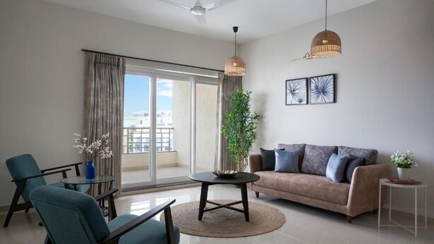 A modern living room with a sofa, chairs, a coffee table, and a large window with curtains. - Paprika Stays (Panaji)