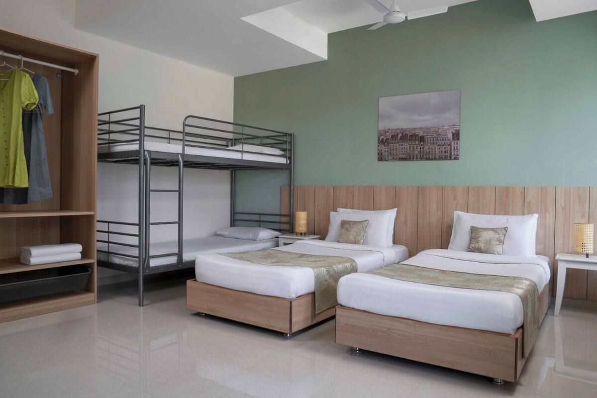Habitación de hotel con literas, dos camas individuales, un armario de madera, una mesita de noche y un cuadro con vista urbana.
