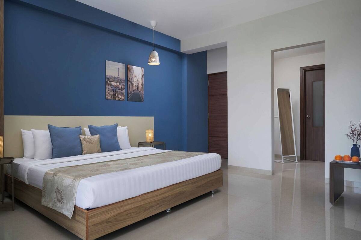 Una habitación de hotel moderna con una cama grande, paredes decoradas en azul y una obra de arte con un paisaje urbano.
