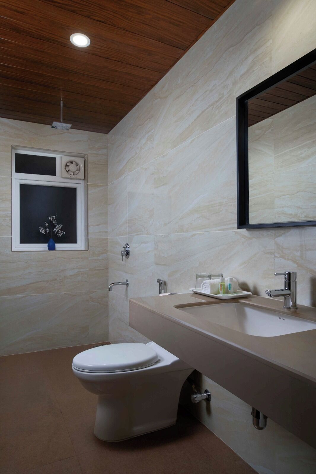 A bathroom with a toilet, a sink with a mirror, and a window with a decorative item.