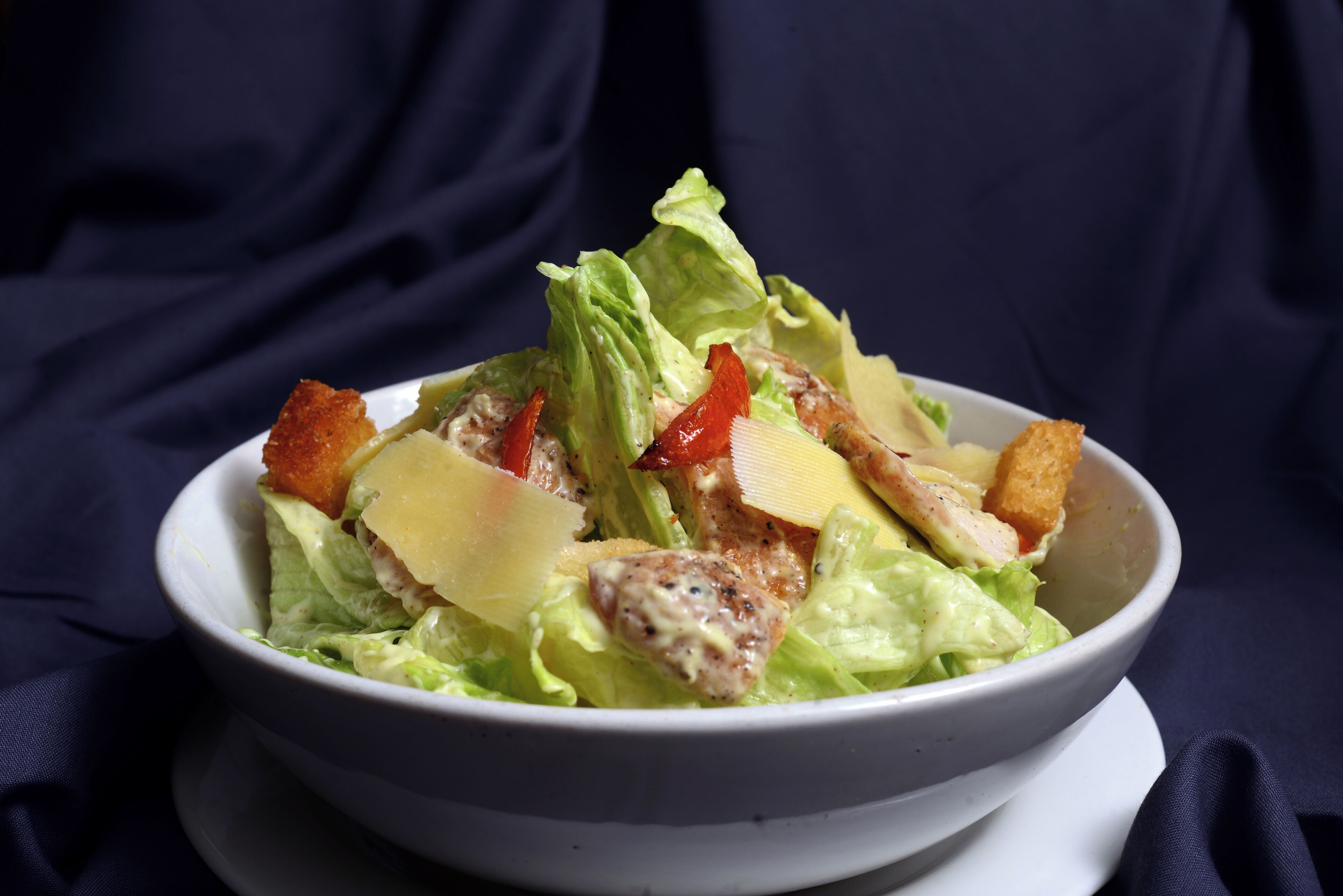 Ensalada con lechuga, crutones y queso sobre un plato blanco.