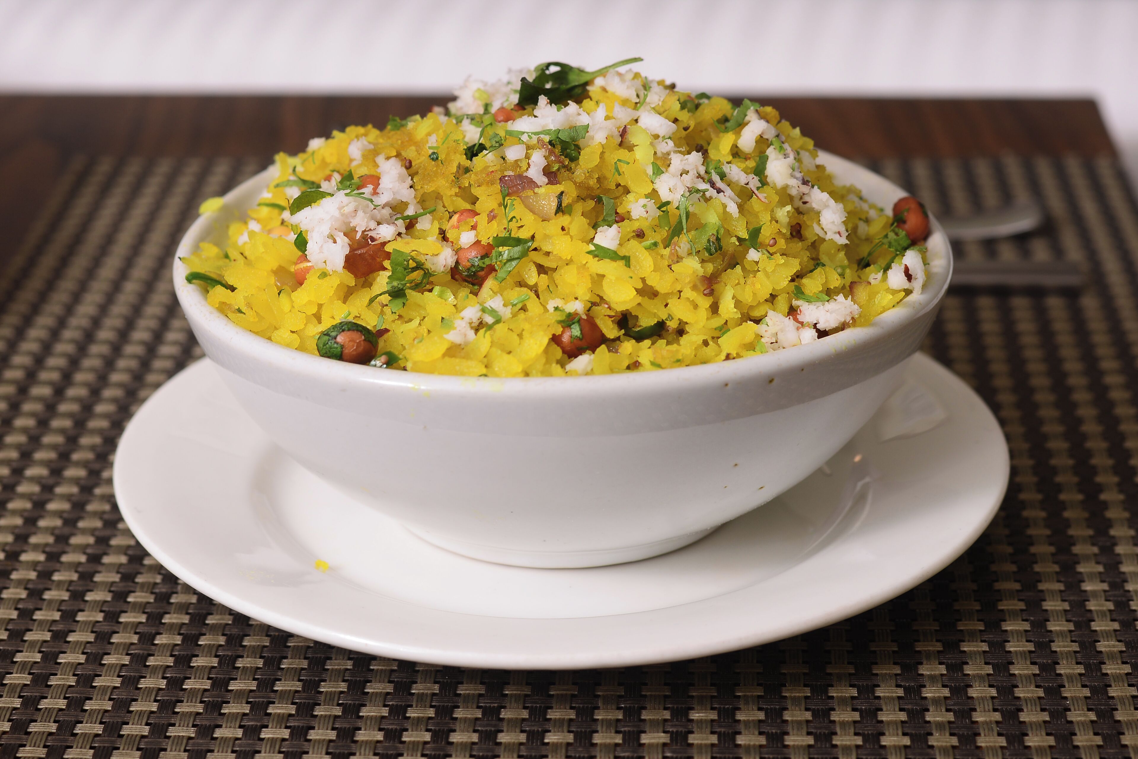 A bowl of yellow rice with herbs and nuts on a white plate.