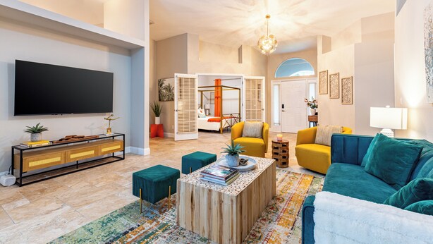 A spacious living room with a flat-screen TV, a wooden coffee table, teal and yellow sofas, and a colorful rug. - Private Pool, Firepit, Game Room | Mins to Beaches | Casa Solara by AvantStay (Naples)