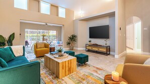 A spacious living room with a large TV, comfortable seating, a coffee table, and a view through a large window. - Private Pool, Firepit, Game Room | Mins to Beaches | Casa Solara by AvantStay (Naples)