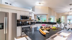 A modern kitchen with stainless steel appliances, a central island with seating, and a view to the dining area. - Private Pool, Firepit, Game Room | Mins to Beaches | Casa Solara by AvantStay (Naples)