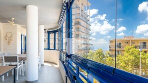 A balcony with a view of the sea, a dining area with a table and chairs, and a large window with a curtain.