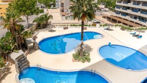 A rooftop swimming pool with multiple sections, palm trees, and lounge chairs.