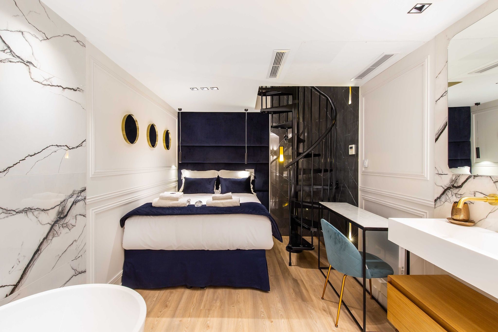A modern bedroom with a bed, a desk, and a chair. There is a staircase leading to an upper level.