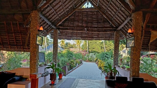 A covered outdoor seating area with a view of a garden. - MEREMETA LODGE (Mafia Island)