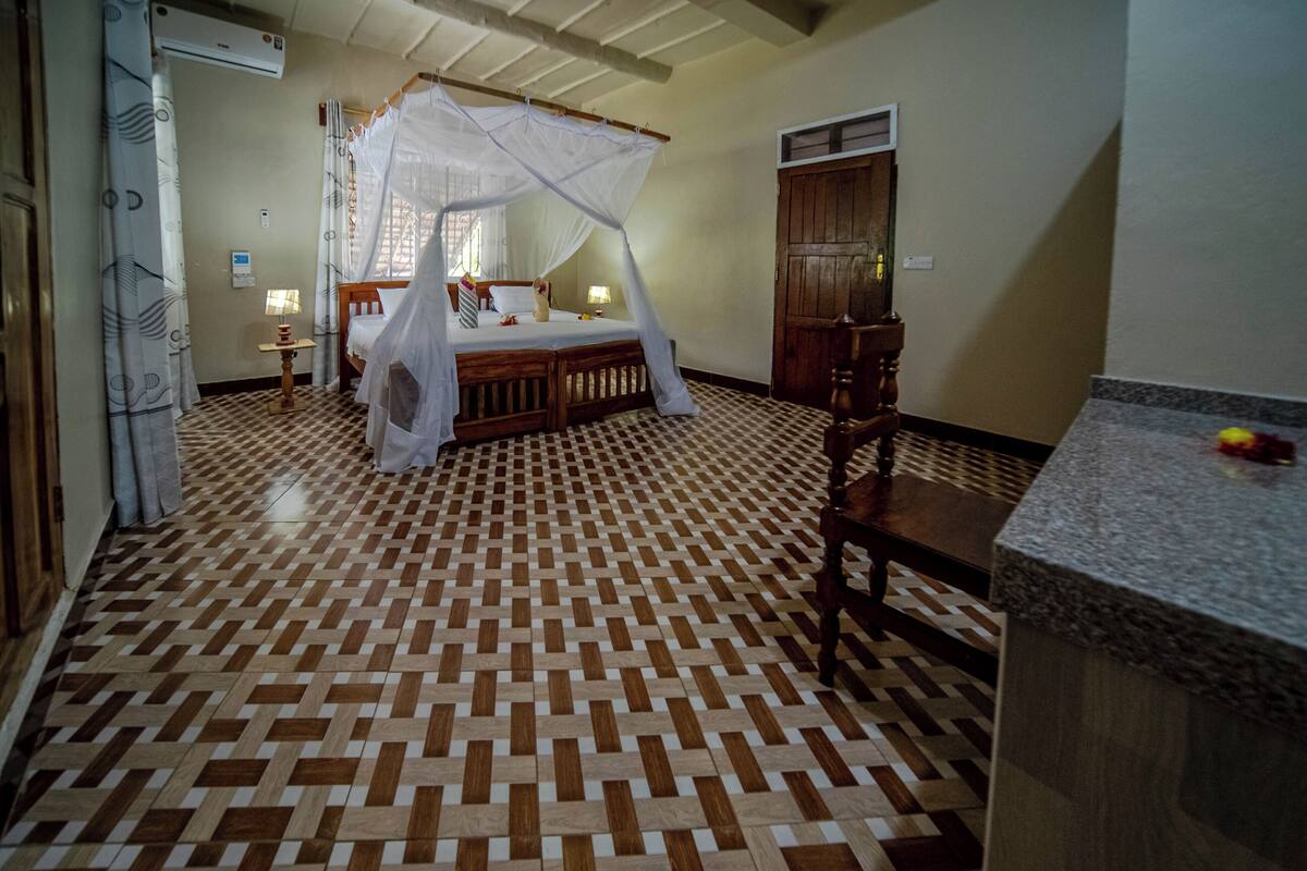 A bedroom with a checkered floor, a canopy bed, a wooden chair, and a small table.