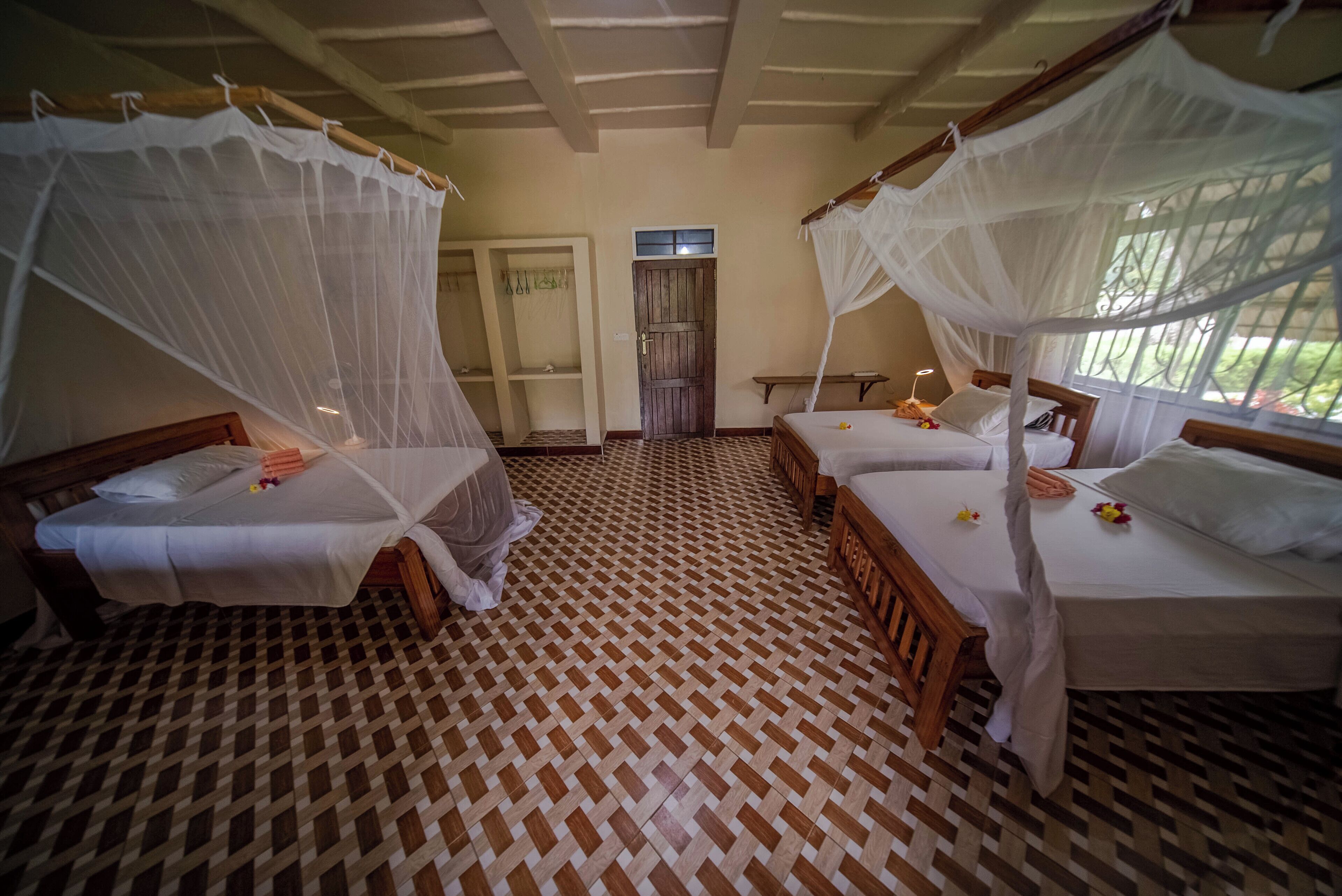 A room with four beds, each with a canopy, and a checkered floor pattern.