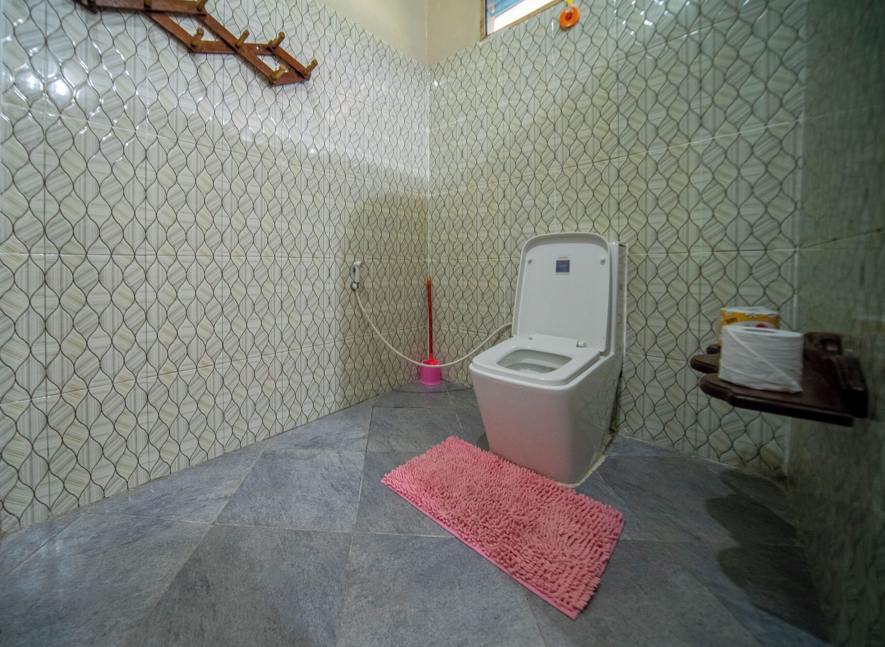 Un bagno piccolo con il water, un tappeto rosa e uno scaffale con prodotti per l'igiene personale.