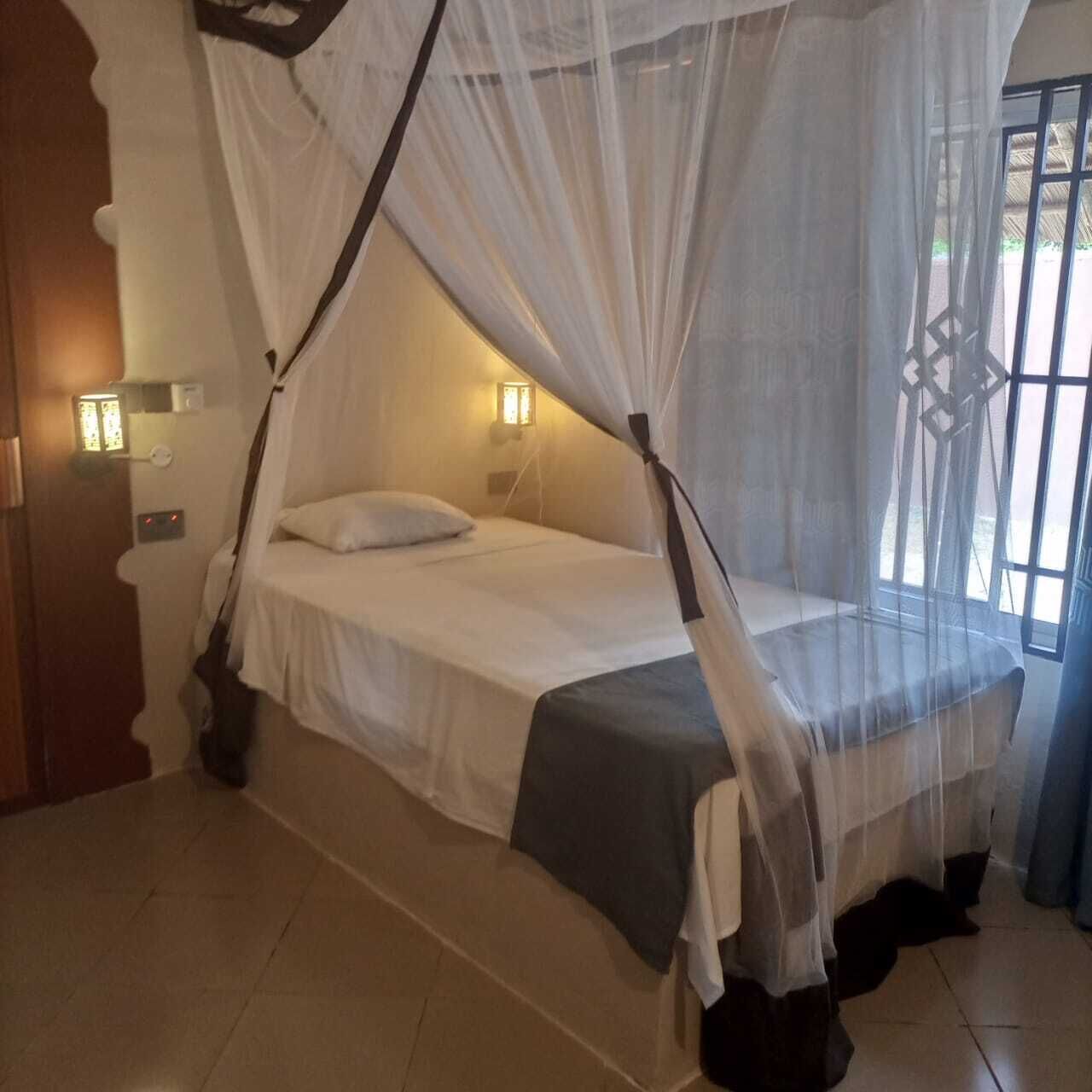 Una cama individual con dosel, lámparas de noche y vistas al exterior a través de una ventana.