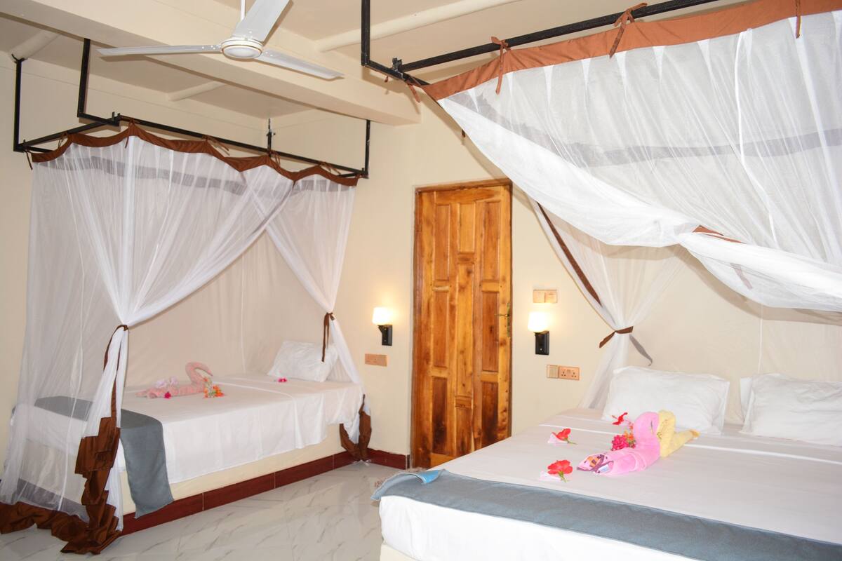 A hotel room with two beds, each with a canopy bedspread and a wooden door.