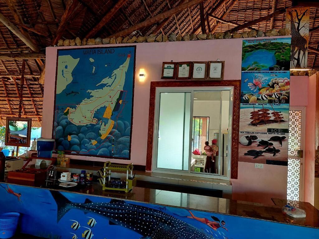 Un espace d’accueil avec une carte de l’île de Mafia, des photos encadrées et un comptoir au design bleu.