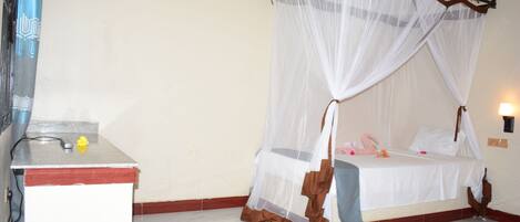 A room with a bed under a canopy, a bedside table, and a wall-mounted lamp.