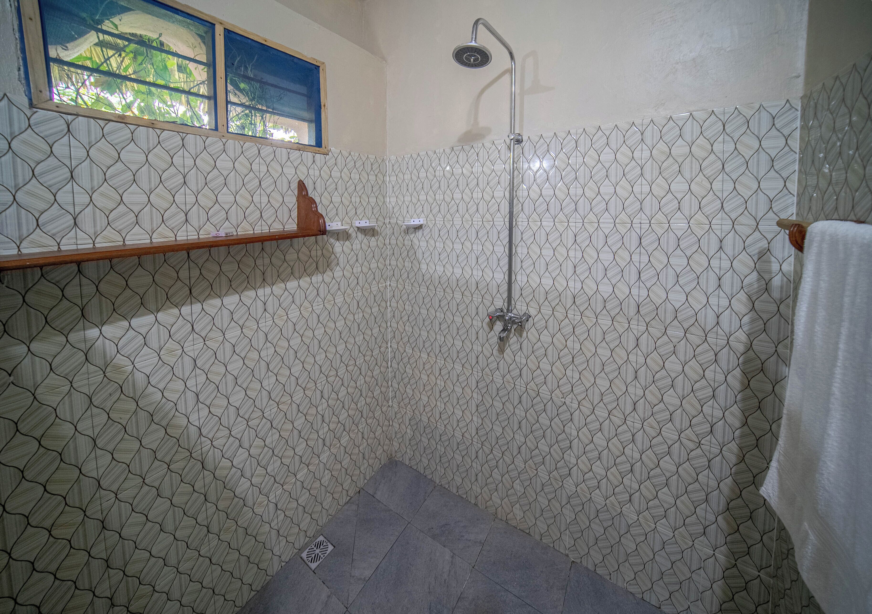 A shower area with a tiled wall, a showerhead, and a shelf.