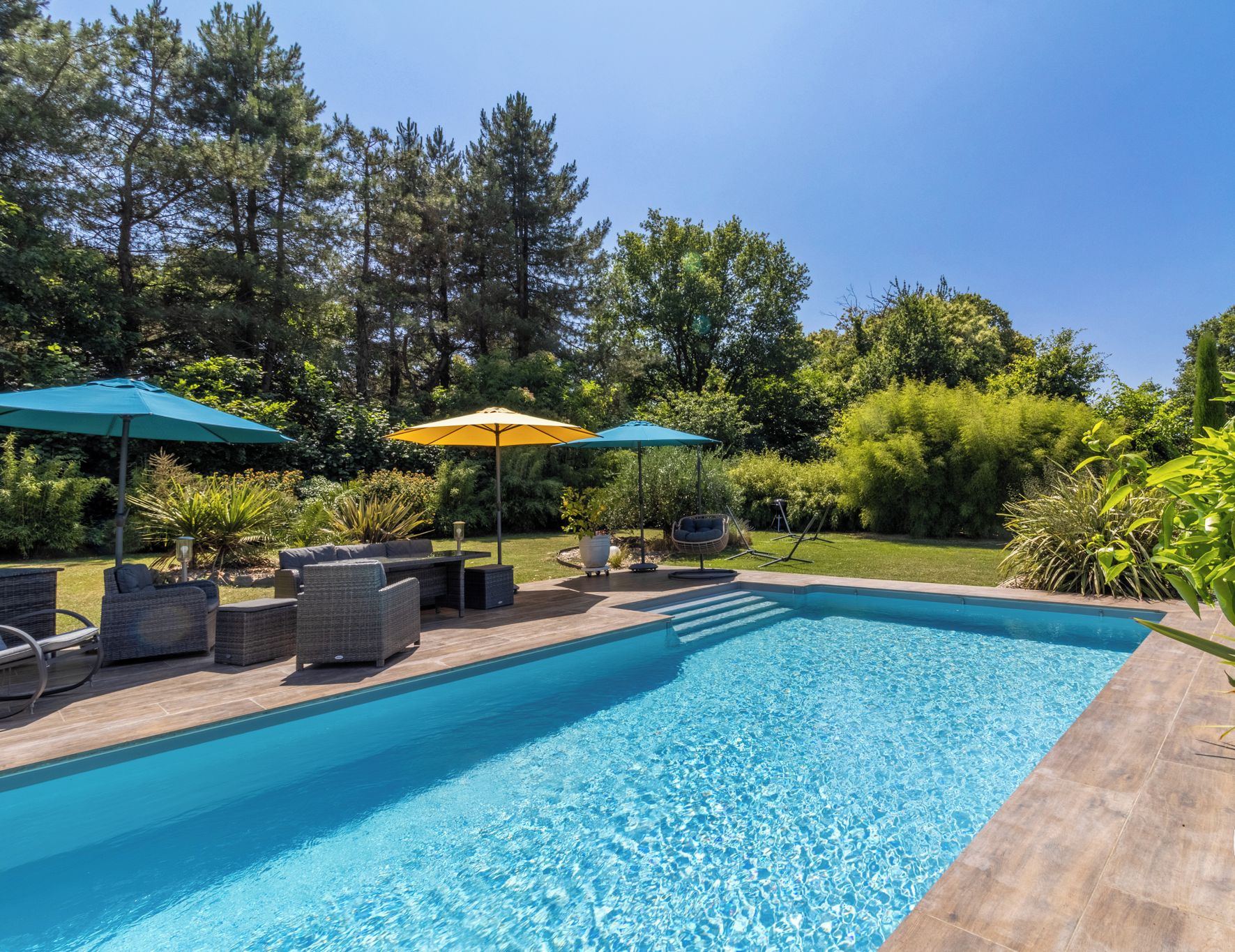 A swimming pool with lounge chairs and umbrellas, surrounded by greenery.