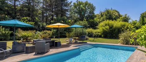 A swimming pool with lounge chairs and umbrellas, surrounded by greenery.