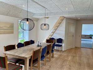 A dining area with a wooden table, striped chairs, pendant lights, and a view of the outdoors.