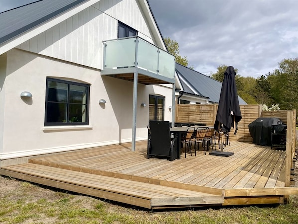 A modern house with a wooden deck, outdoor furniture, and a barbecue area.