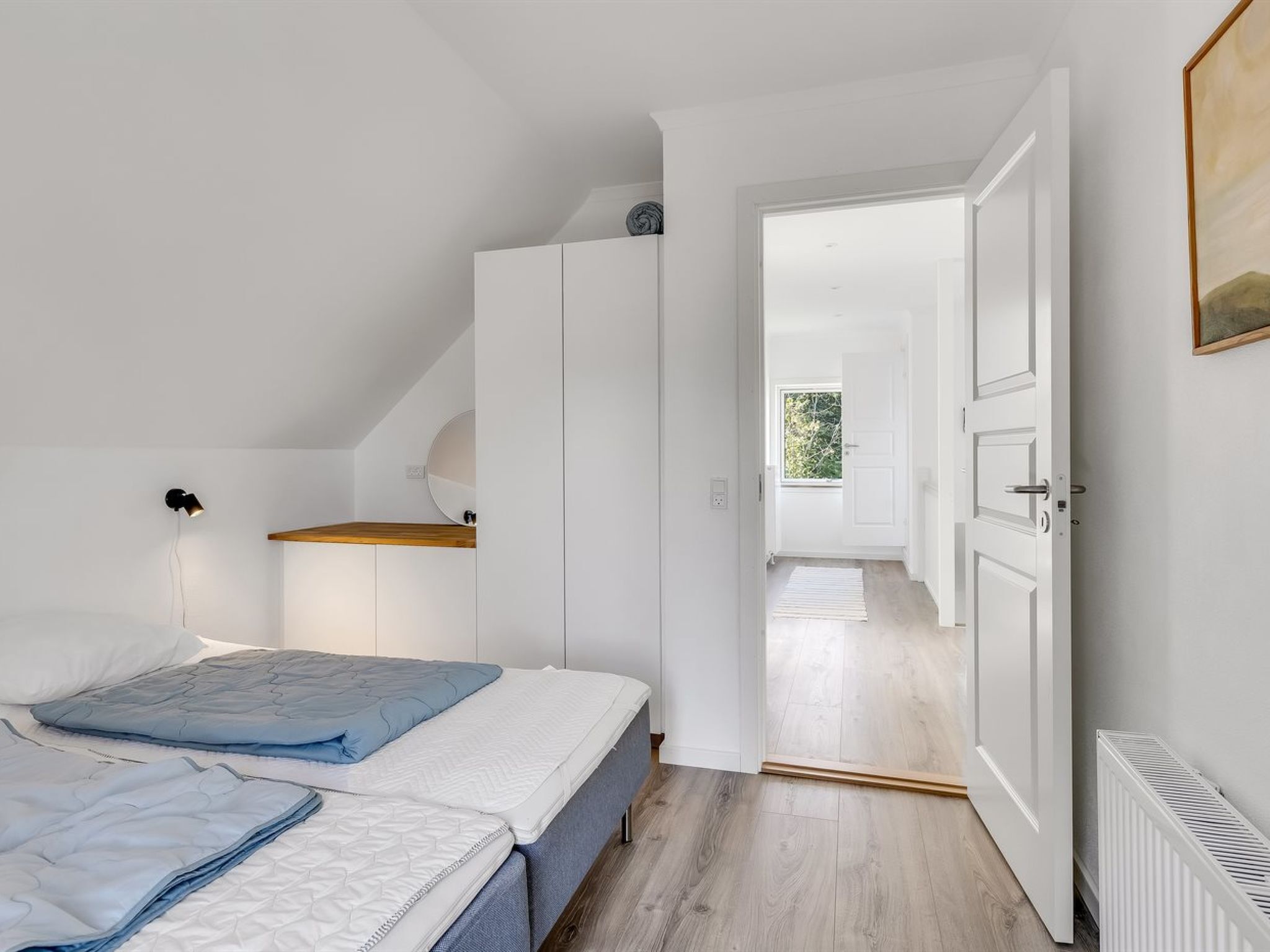 A bedroom with two beds, a wardrobe, a desk, and a view of the outside.